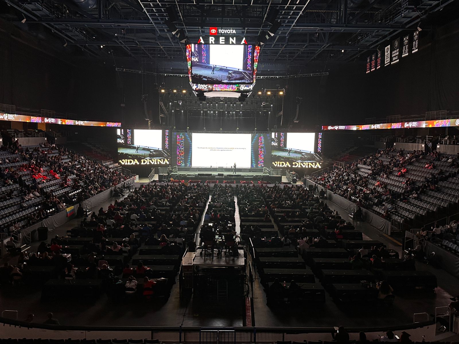 Wide view of an arena conference with a large crowd, three LED screens and an overhead video cube