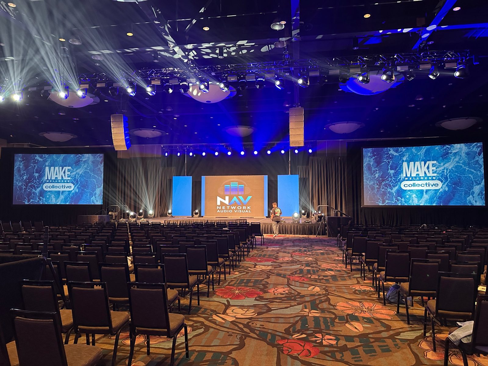 Network Audio Visual logo on the LED wall in a full conference ballroom with stage lighting and line array speakers